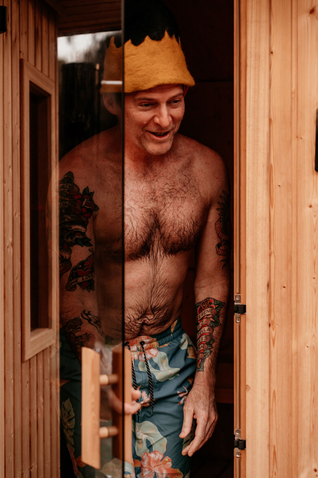 A member in a felt sauna hat stepping out of the sauna door, smiling