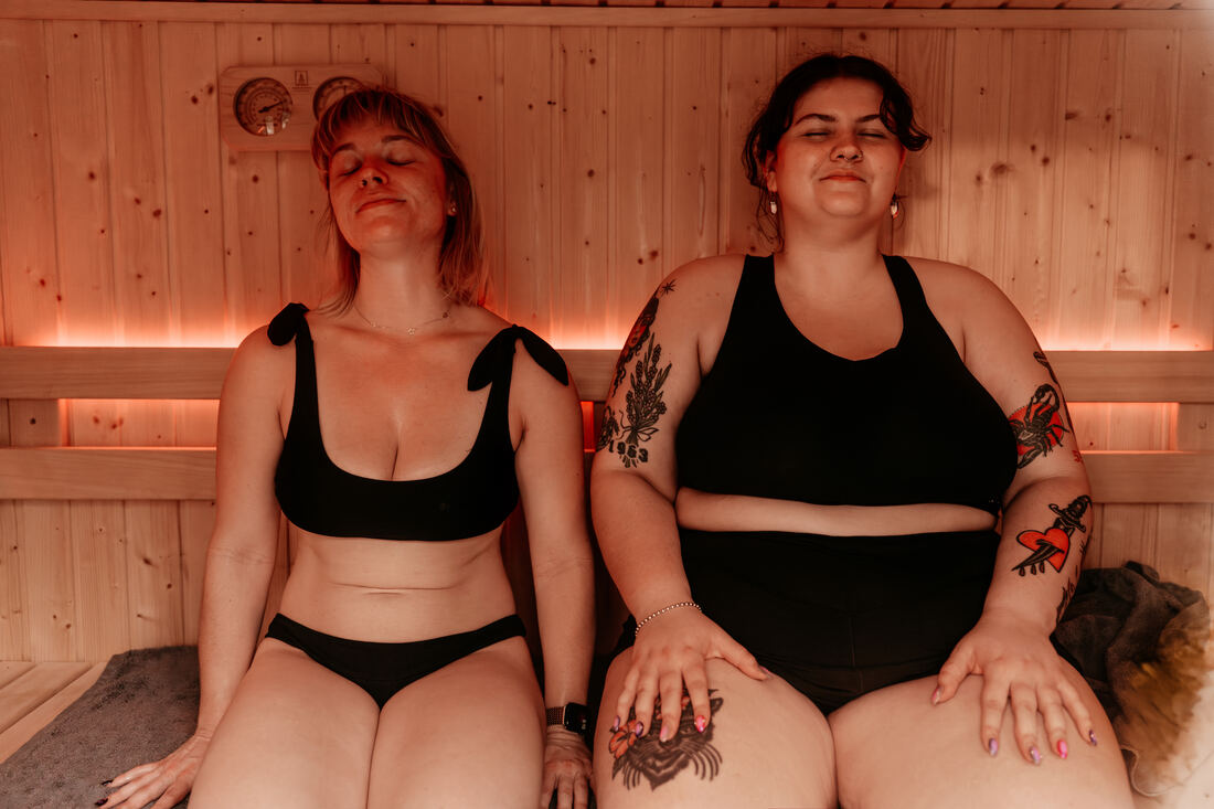 Two members sitting with eyes closed in the warm light of a RITUAL Finnish sauna
